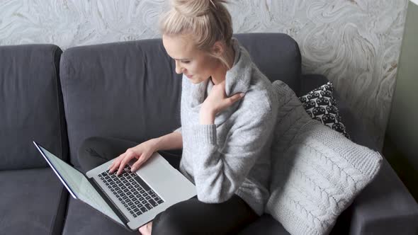 Middle Aged Woman Sitting on Sofa in Her Living Room and Working on Laptop