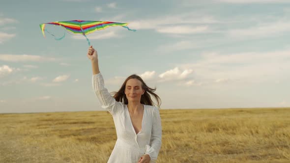 Woman in a Beautiful Dress Flying on a Rainbow Kite on a Field on a Sunny Day