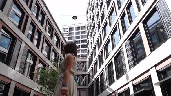 Young attractive business woman looks around turning between tall office buildings in financial dist