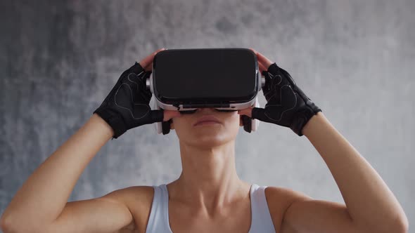 Young and sporty girl in sportswear is doing exercises at home using virtual reality helmet.