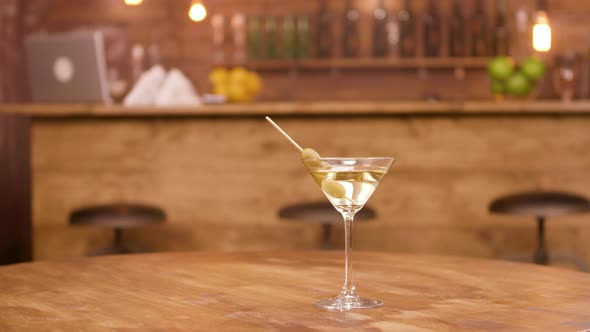 Parallax Shot of a Martini Glass on an Empty Wooden Table with Bar Counter on the Background