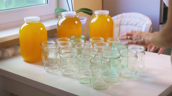 Woman Pours Honey Into Transparent Jars on a White Table