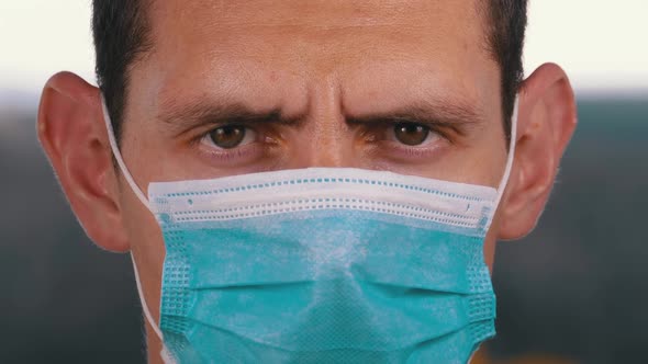 Young Man in a Medical Protective Face Mask Looking at the Camera on the Street Background