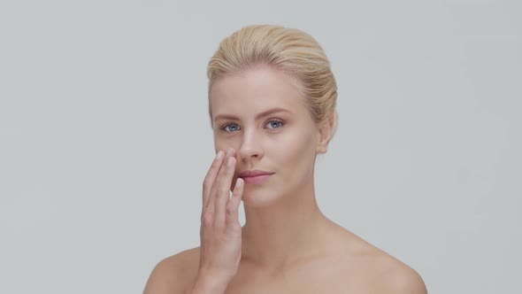 Studio portrait of young, beautiful and natural blond woman applying skin care cream. F