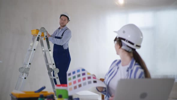 Woman in Hard Hat and Eyeglasses with Color Palette is Choosing New Room Design While Sitting at