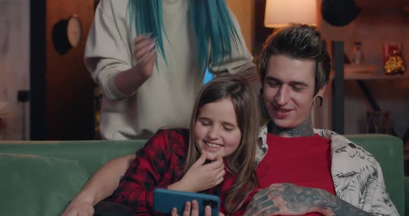 Millennial Father with Tattoos and Piercing and His Teen Daughter Looking on Phone Screen and