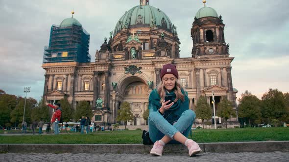 BERLIN, GERMANY - October 2018: Tourist Girl in the Autumn Uses a Mobile Phone While Sitting on the