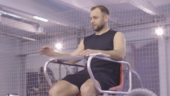 Portrait of Confident Caucasian Judge Sitting on Referee Chair in Gym and Talking. Positive