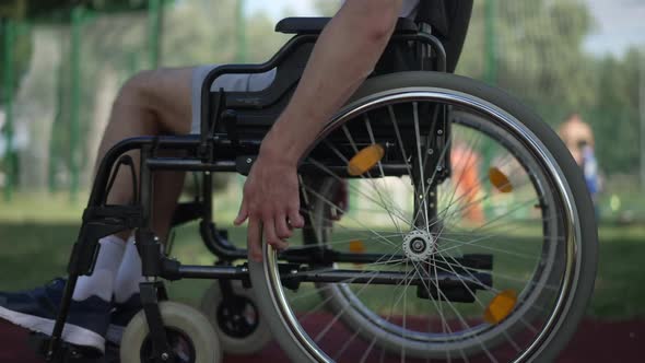 Side View Male Hands Rolling Wheelchair Wheels Riding Fast in Sunshine Outdoors