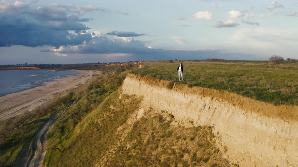 Tracking Aerial Shot of Young Woman Enjoying Sunset in Field Near the Cliff During Beatiful Sunset