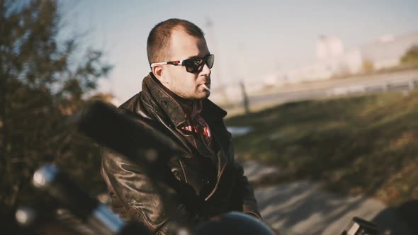 Young Man Motorcyclist Smokes a Cigarette While Sitting on a Motorcycle