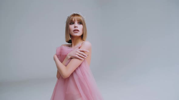 Attractive young Caucasian woman with a Bob haircut in a pink dress on a white background	