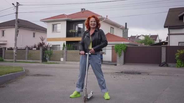 Wide Shot Satisfied Smiling Retro Woman Standing with Kick Scooter Looking at Camera