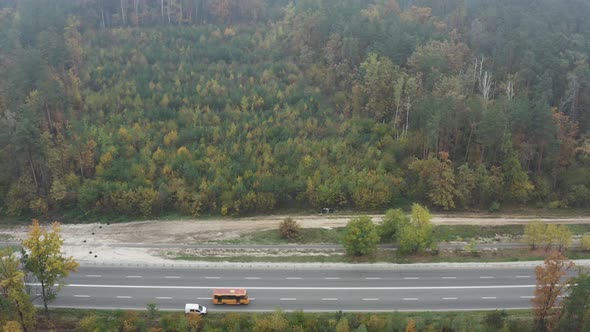 Highway with passing cars in the autumn forest from aerial view.