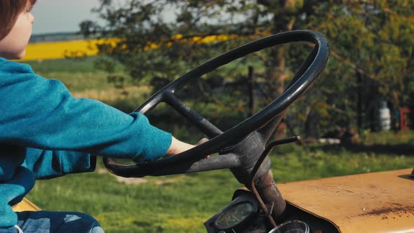 Boy on the old yellow tractor, pretending to be driving. He turns steering wheel. He is playing. Bea