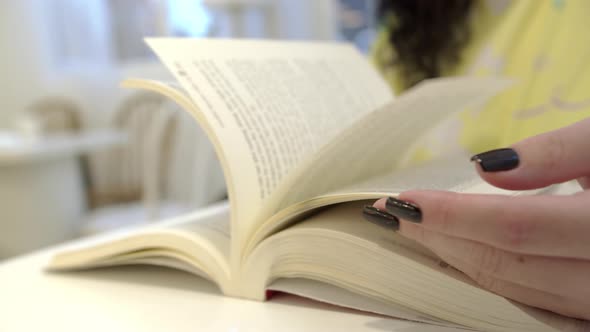 Girl is Reading a Book at the Table a Woman is Turning the Pages of a Book Close Shot