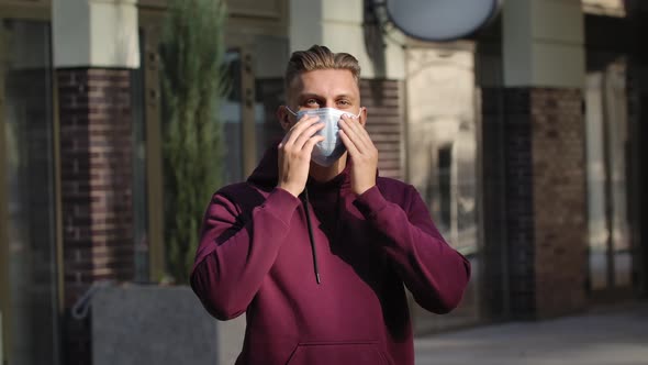 Portrait of Young Man Looking at the Camera and Putting Medical Mask on Face for Protection Against