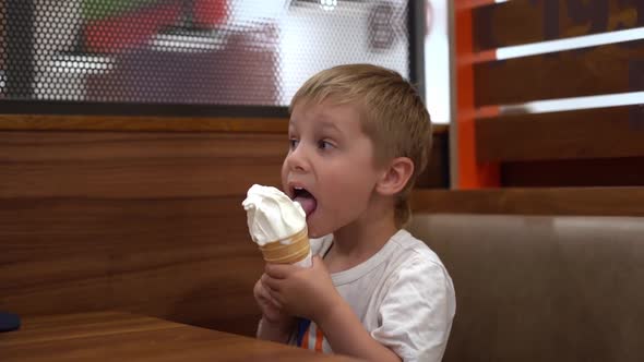 Adorable Little Caucasian Boy Eating Icecream Cone at the Table in Cafe