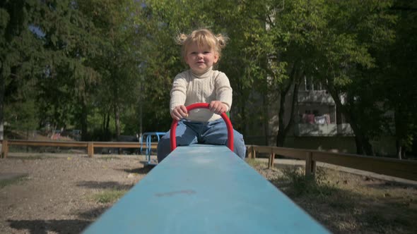 Little Cute Blond Girl Rides Teeter Totter at Playground