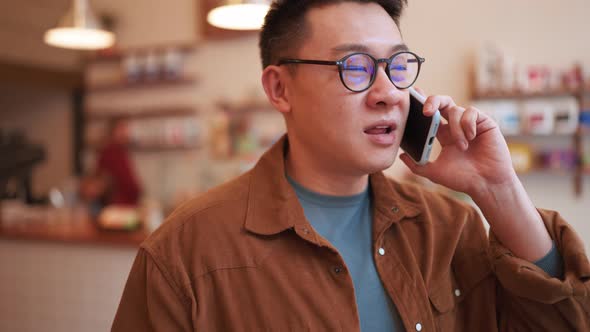 Cheerful Asian young man wearing eyeglasses talking on phone