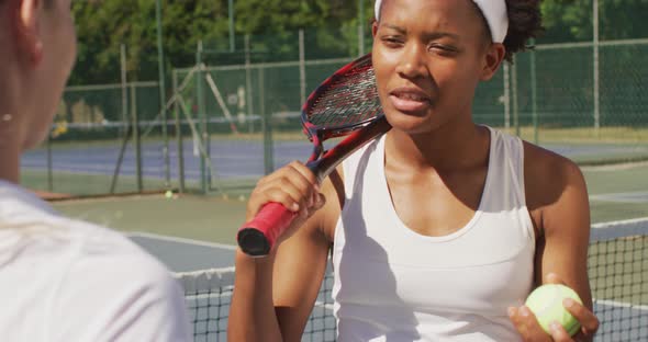 Video of happy african american female tennis player holding racket and talking with friend