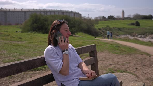 The Girl Sits on a Bench Near the Ocean and Talks on the Phone