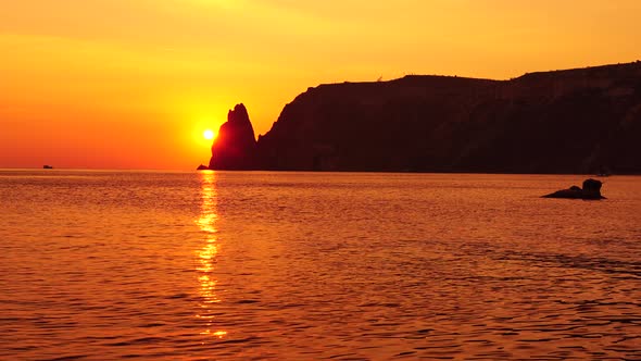 A Red Burning Sunset with the Silhouette of a Cliff Over the Sea