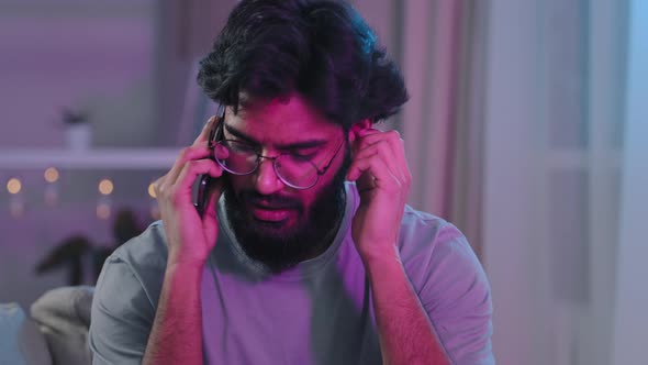 Arabic Indian Bearded Man with Glasses Talking on Phone at House Party Sitting on Sofa Neon Light