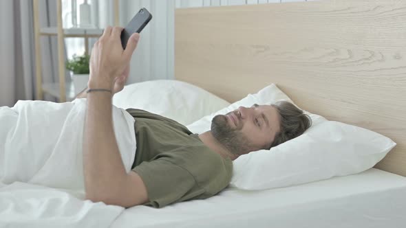 Young Man Scrolling His Cellphone in Bed