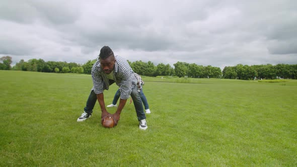 Cheerful Black Little Son and Dad Playing American Football Outdoors