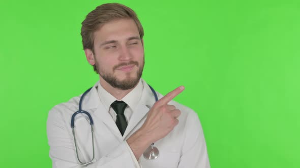 Young Doctor Pointing on Side on Green Background