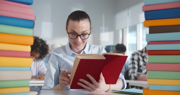 Young Woman in Glasses Reading Textbook in Classroom