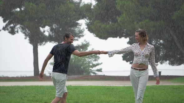 A Romantic Couple Joyfully Dancing Around Each Other in the Pouring Rain at a Park, Slow Motion, Sta