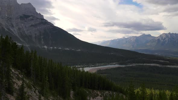 Slow aerial push inement above the Canadian Rocky mountains covered by vast forests. Cloudy Sky duri