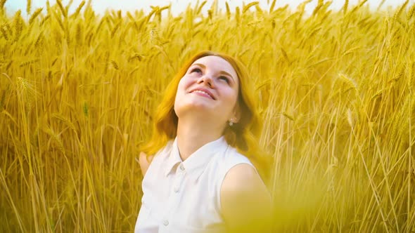 Smiling red haired girl daydreaming in wheat field in harvest season