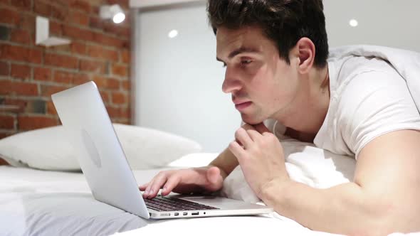 Young Man in Bed Working on Laptop and Reacting to Success