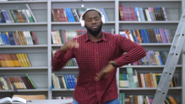 Joyful Black Man in Headphones Dancing in Library
