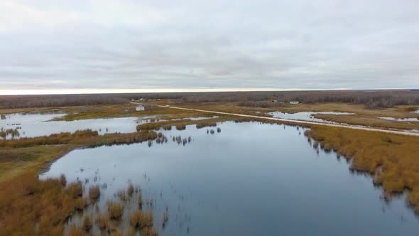 Aerial footage of lake, thicket, road, small settlement and cloudy horizon (Manitoba, Canada)