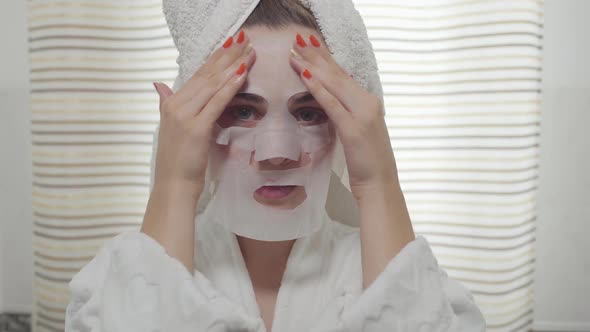 Cheerful Young Woman Looking in the Camera Applying the Sheet Mask on Her Face in the Bathroom