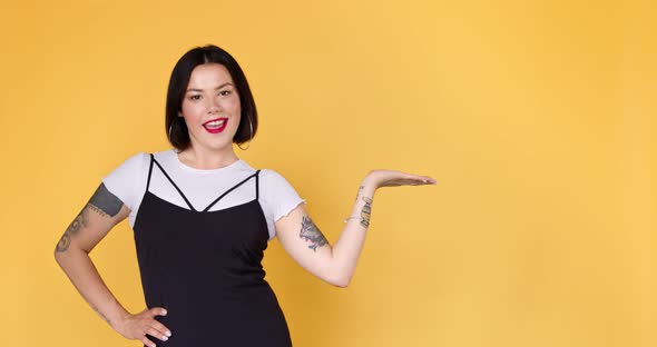 Stylish woman with tattoo holding copy space on palm and pointing at workspace