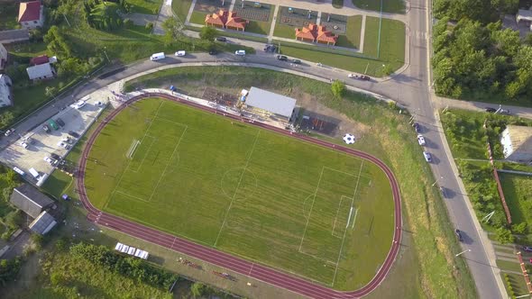 Aerial view of a football field on a stadium covered with green grass in rural town area.