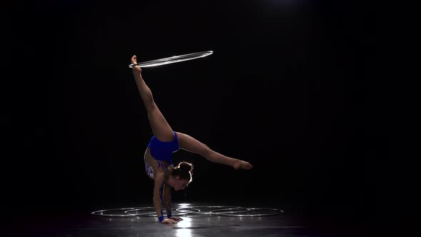 Gymnast in a Bright Outfit Twists a Hoop on Her Arm and Then on Her Leg. Black Background