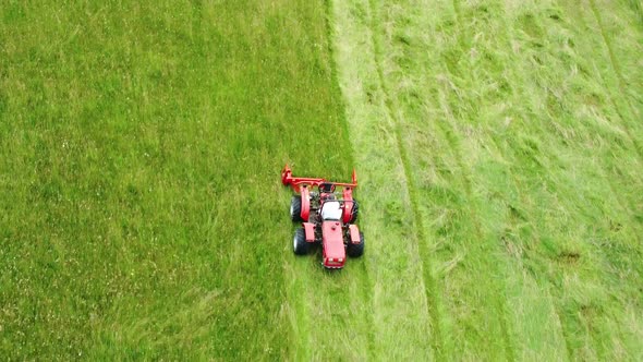 Red lawnmower tractor moving straight parallel rows of green grass. Aerial 4k view.