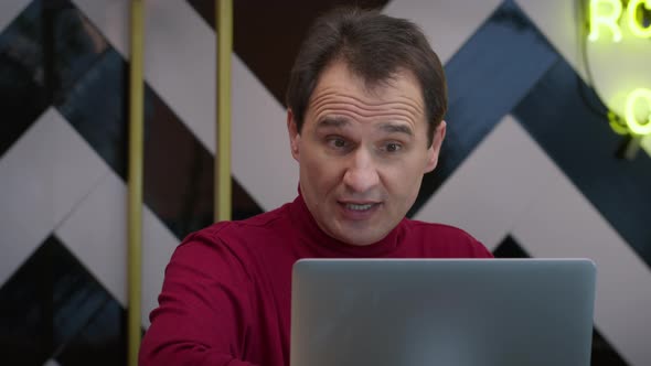 Smiling Handsome Middleaged Man Chutting in Cafe with Laptop and Cup of Coffee