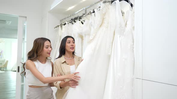 4K Asian lesbian couple choosing wedding dress in bridal shop together.