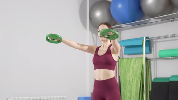 a Beautiful and Slender Young Woman Does Exercises with Weights in the Gym