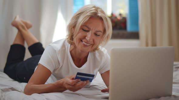 Positive Senior Woman Checking Credit Card Balance Via Laptop at Home