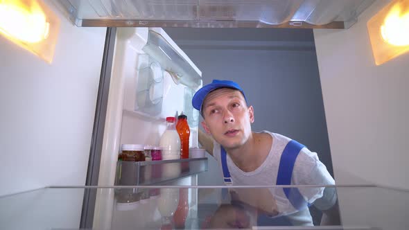 repairman looks into refrigerator, puts his hands on his head and is surprised