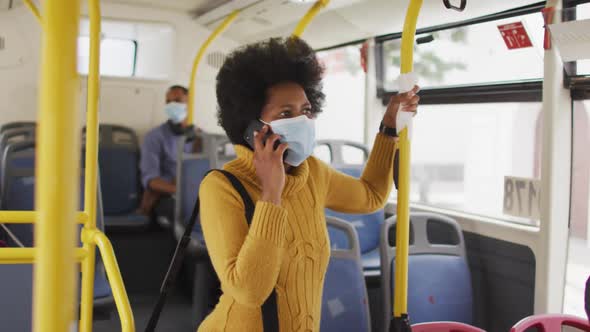 African american businesswoman with face mask talking on smartphone and standing in bus