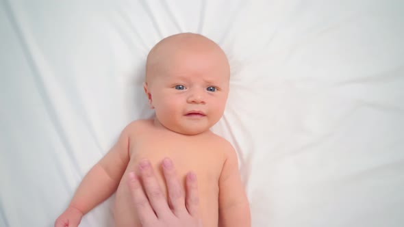 Hands Do Massage to Baby on White Sheet for a Healthy Tummy